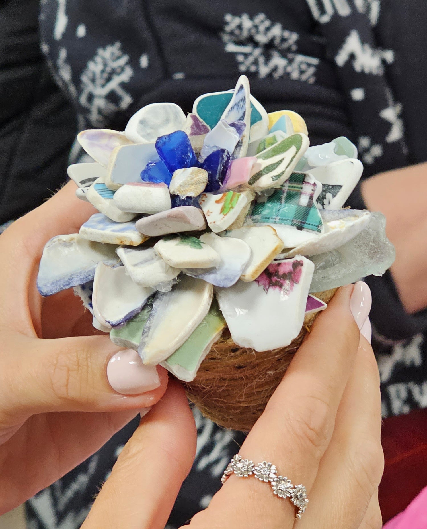 A hand holding a ceramic tree with mosaic flower design pot