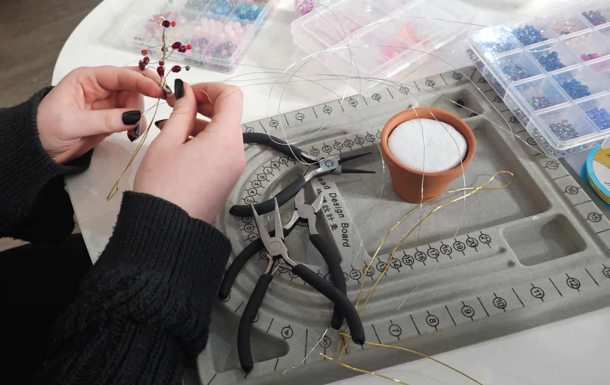 Person working with jewelry-making tools and materials on a table.
