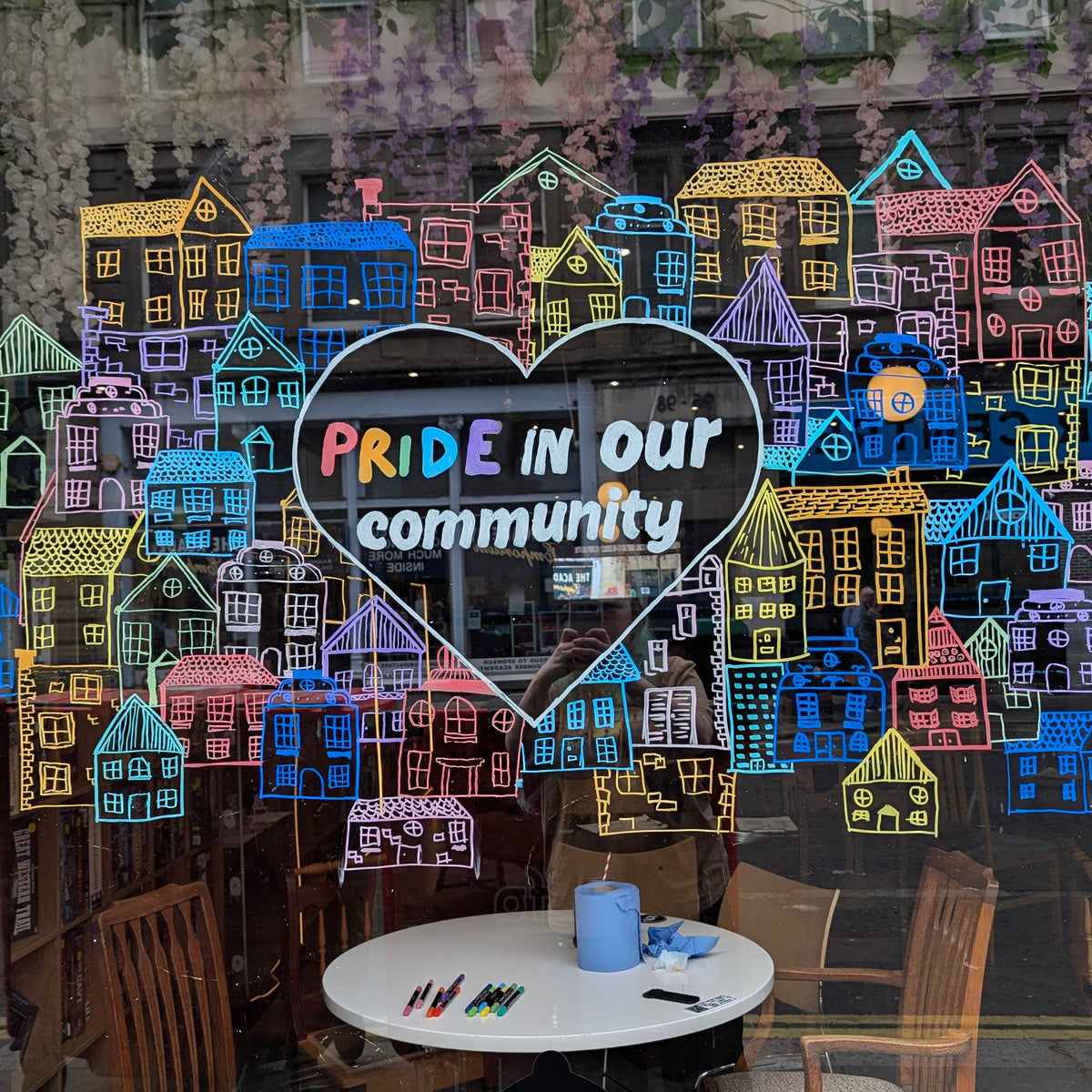 Our café window with a hand drawn Pride in our community display and colourful houses